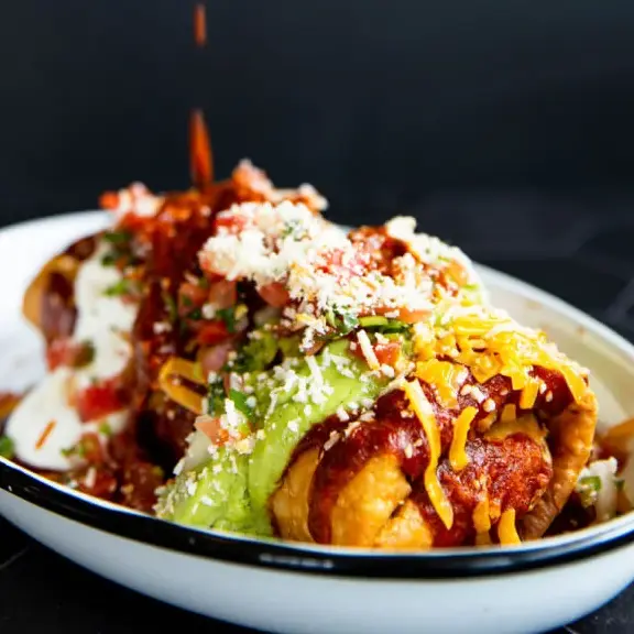 Rolled tacos topped with red sauce, guacamole, sour cream, and cheese